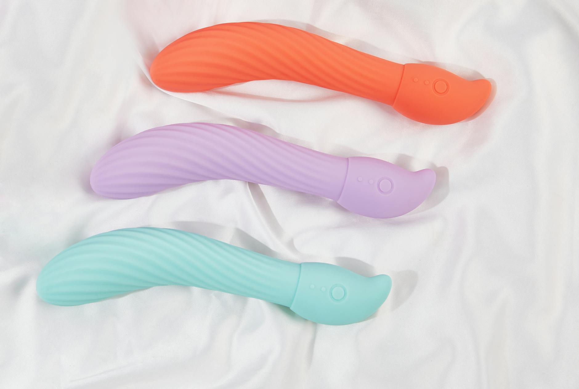 Three colorful clitoral vibrators on soft white fabric, showing texture and design.