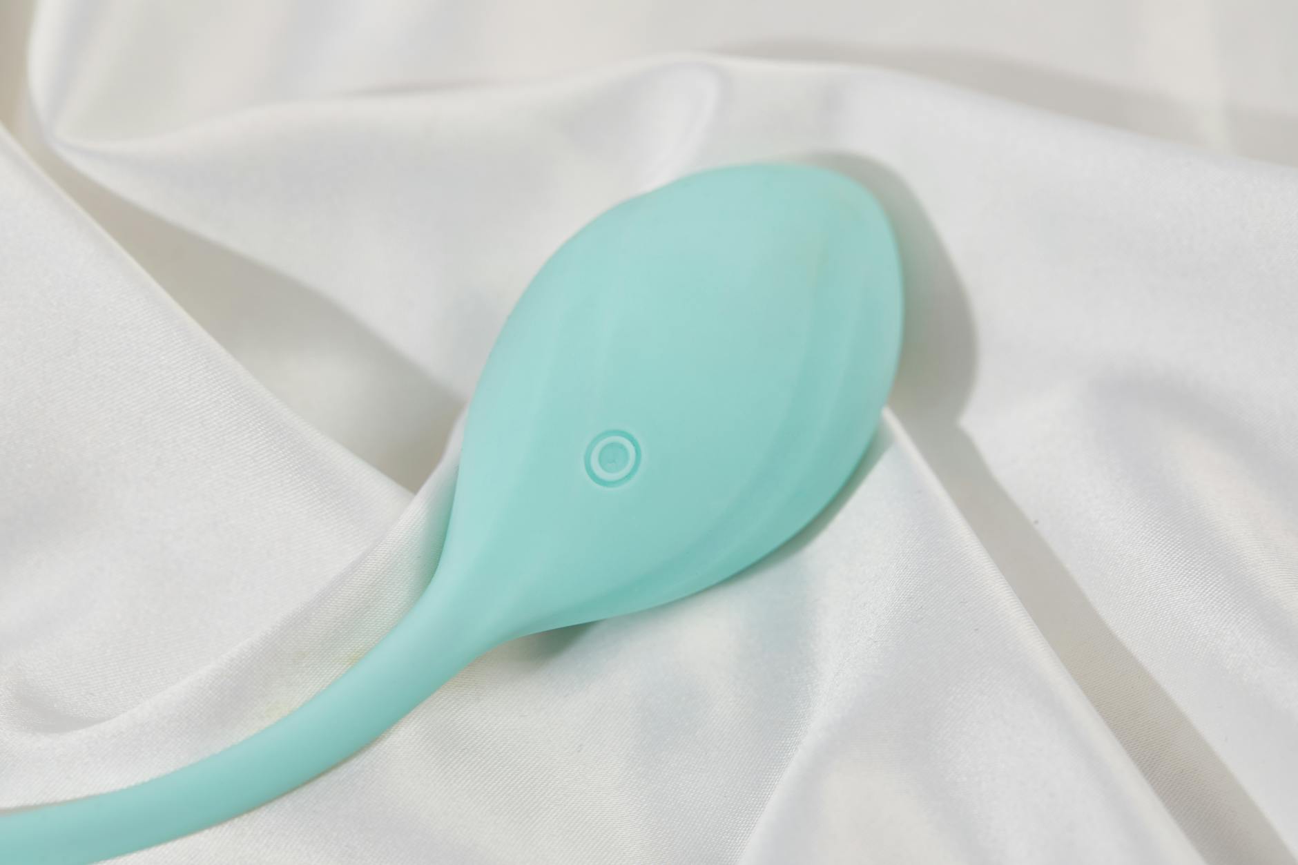 A teal vibrator resting on white silk fabric