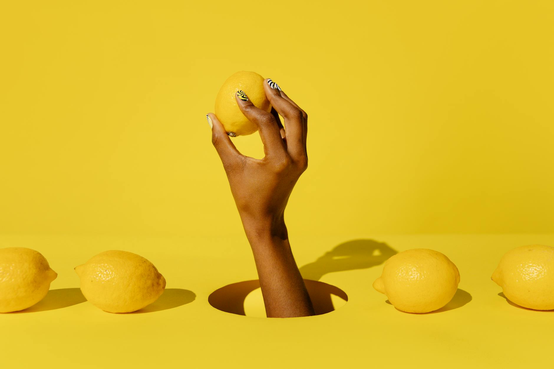A hand holding a fresh lemon against a bright yellow background, representing renewal and sensitivity restoration