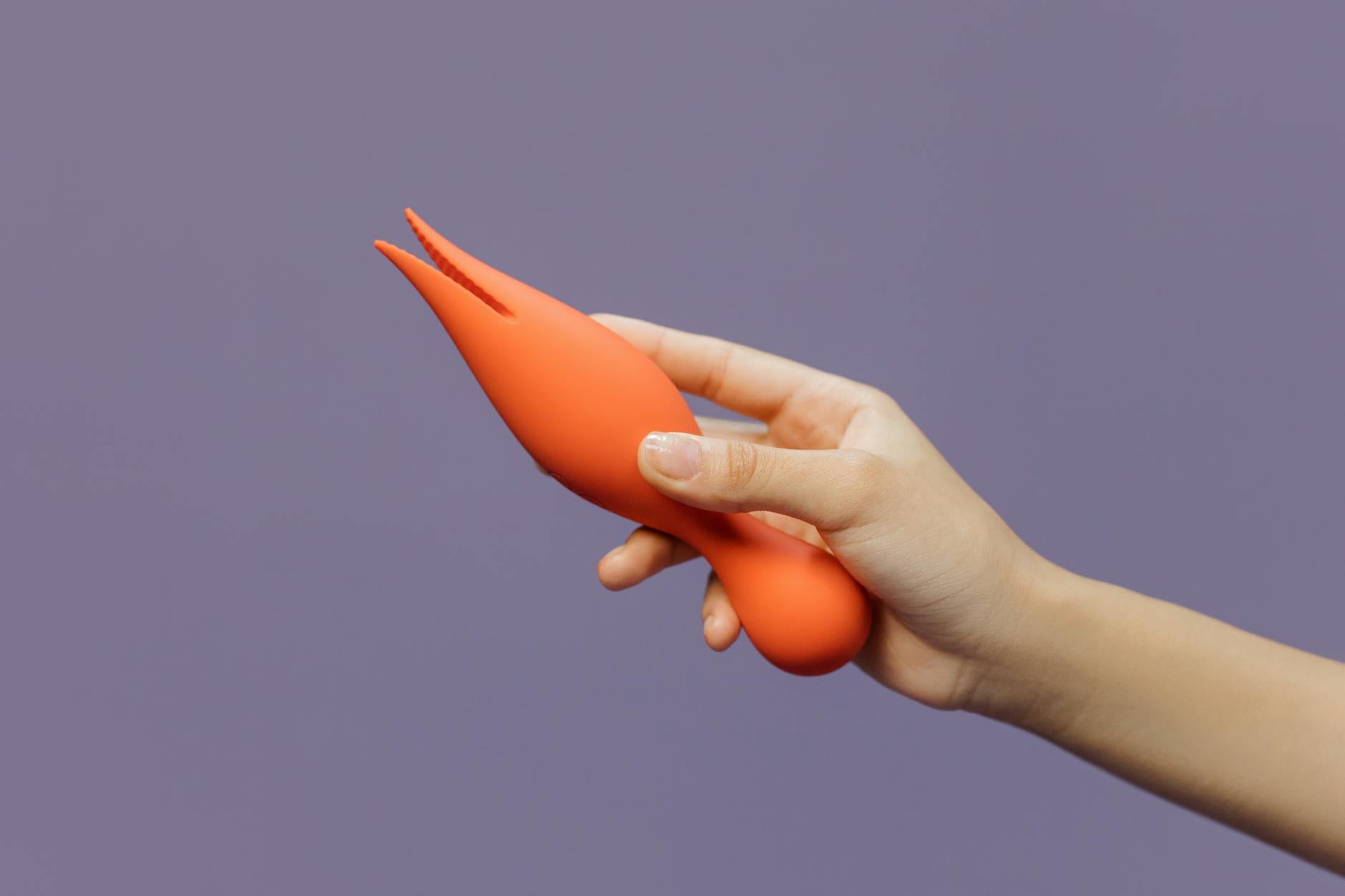 Close-up of an orange vibrator held against a minimalistic backdrop, representing self-directed pleasure