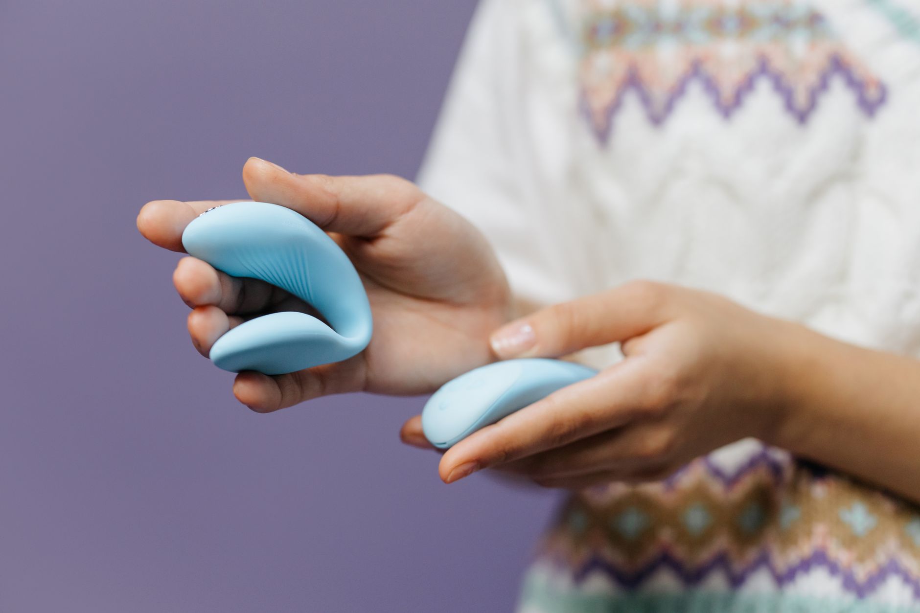 A person holding a sleek blue vibrator against a purple background
