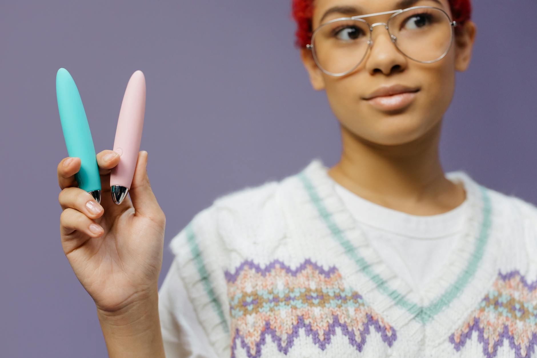 A woman holds two colorful vibrators, exploring clitoral stimulation options