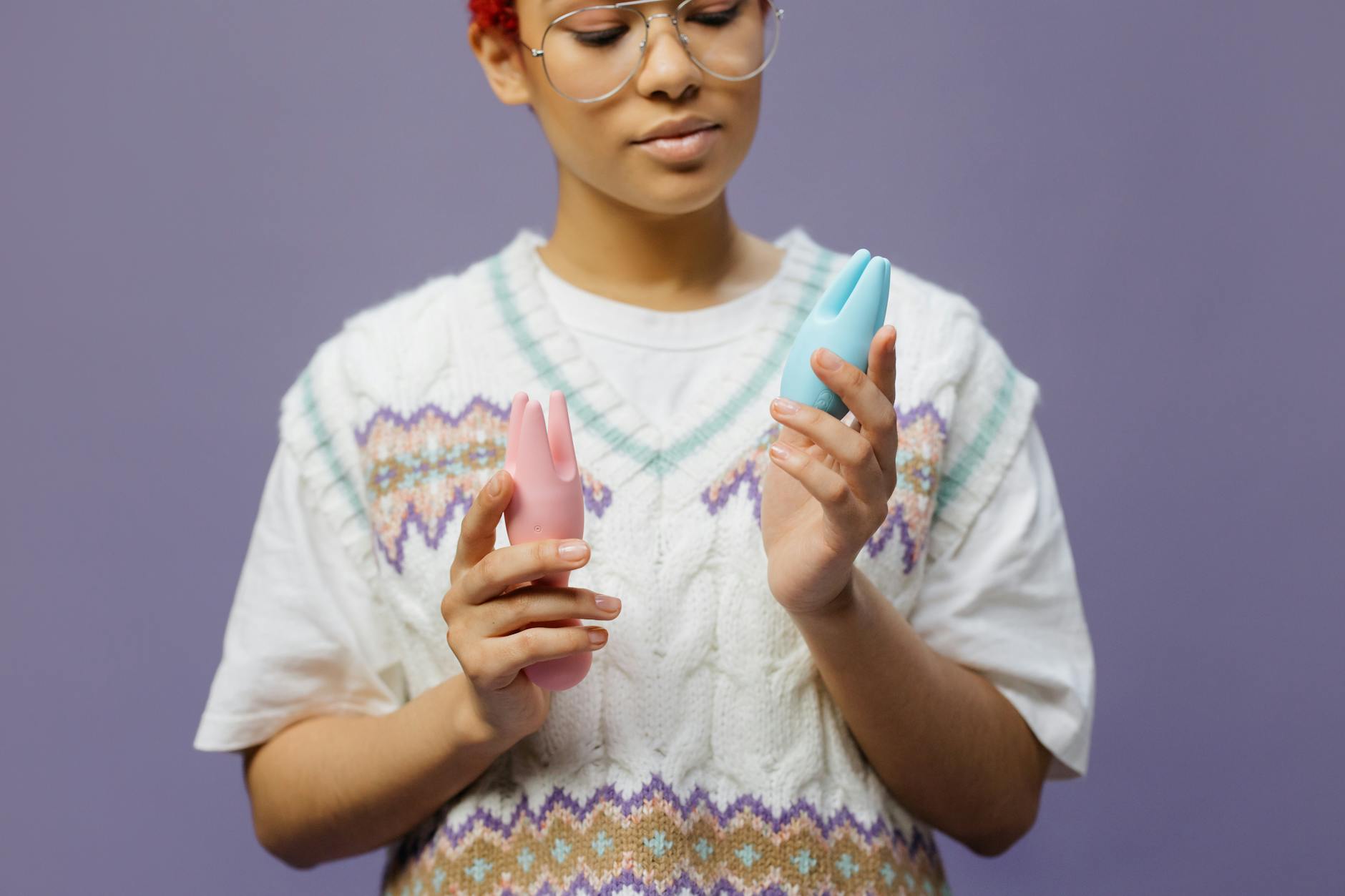Woman holding blue and pink vibrators thoughtfully, representing the journey of reconnecting with pleasure.