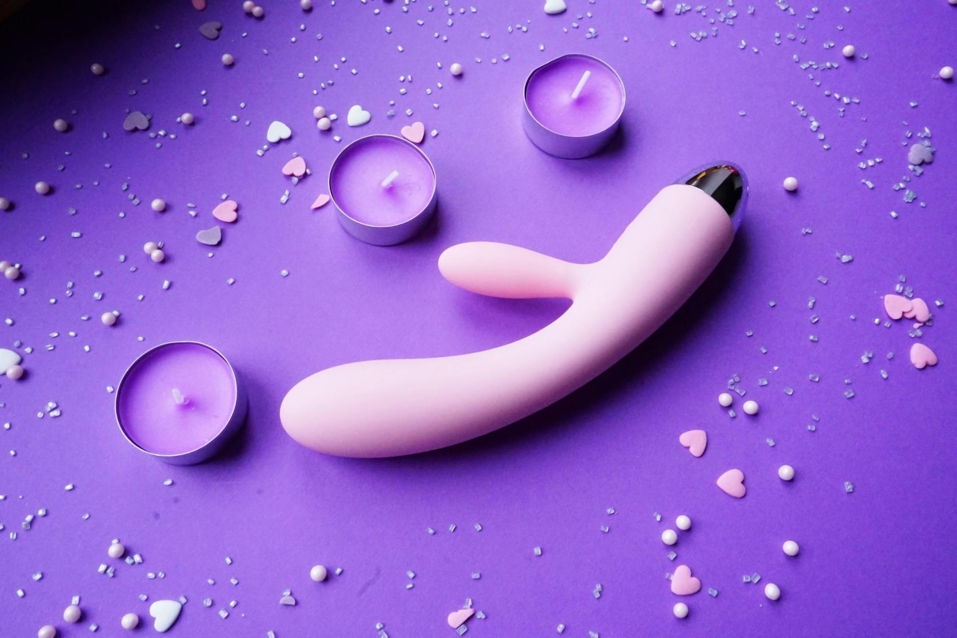 Pink lemon vibrator on purple background with candles and confetti, representing mature sensuality